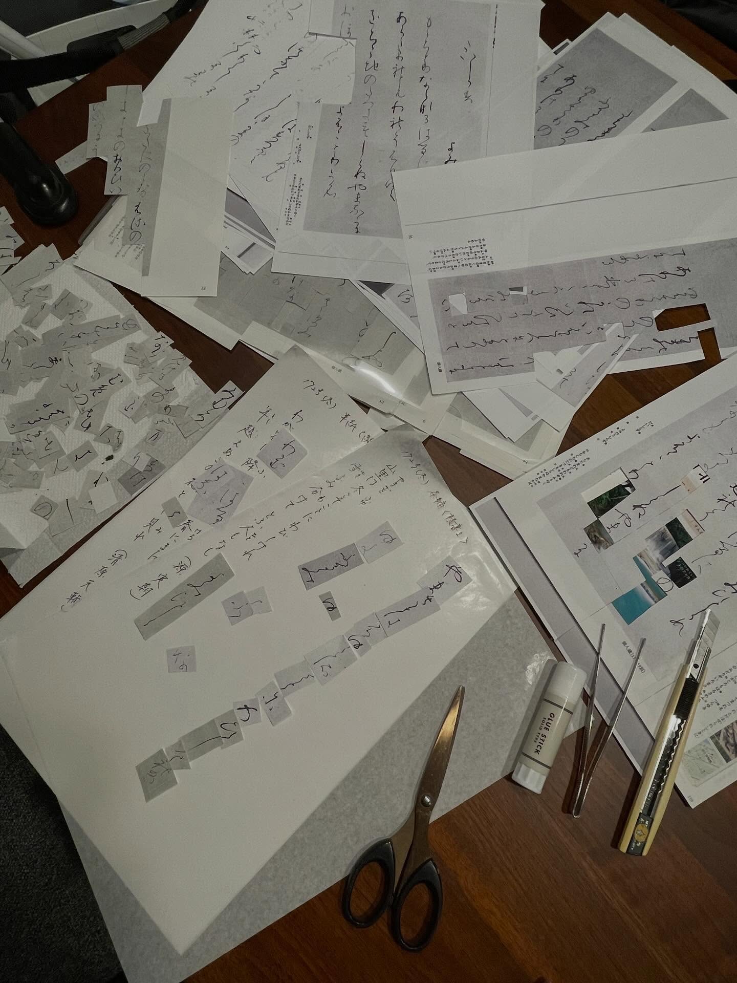 古典から選んだ仮名の文字、紙、筆やはさみが並ぶ講師の集字作業の机
